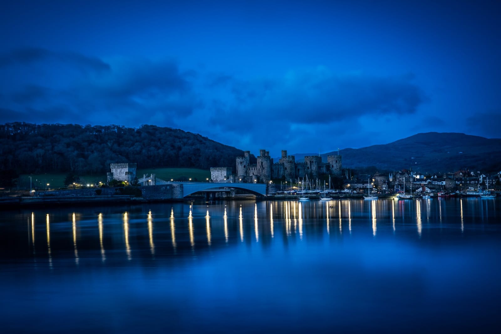 Conwy Castle and the estuary at blue hour, harbour lights reflected in the water