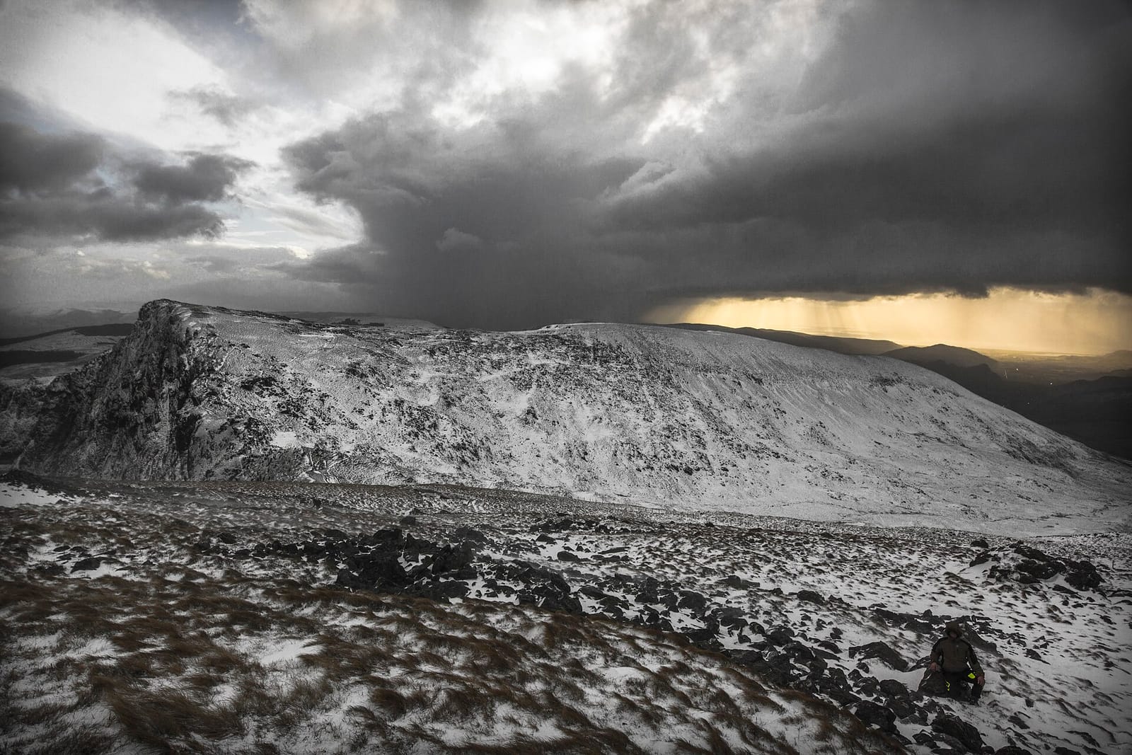 Snow-covered Snowdonia mountains beneath a dramatic, stormy winter sky