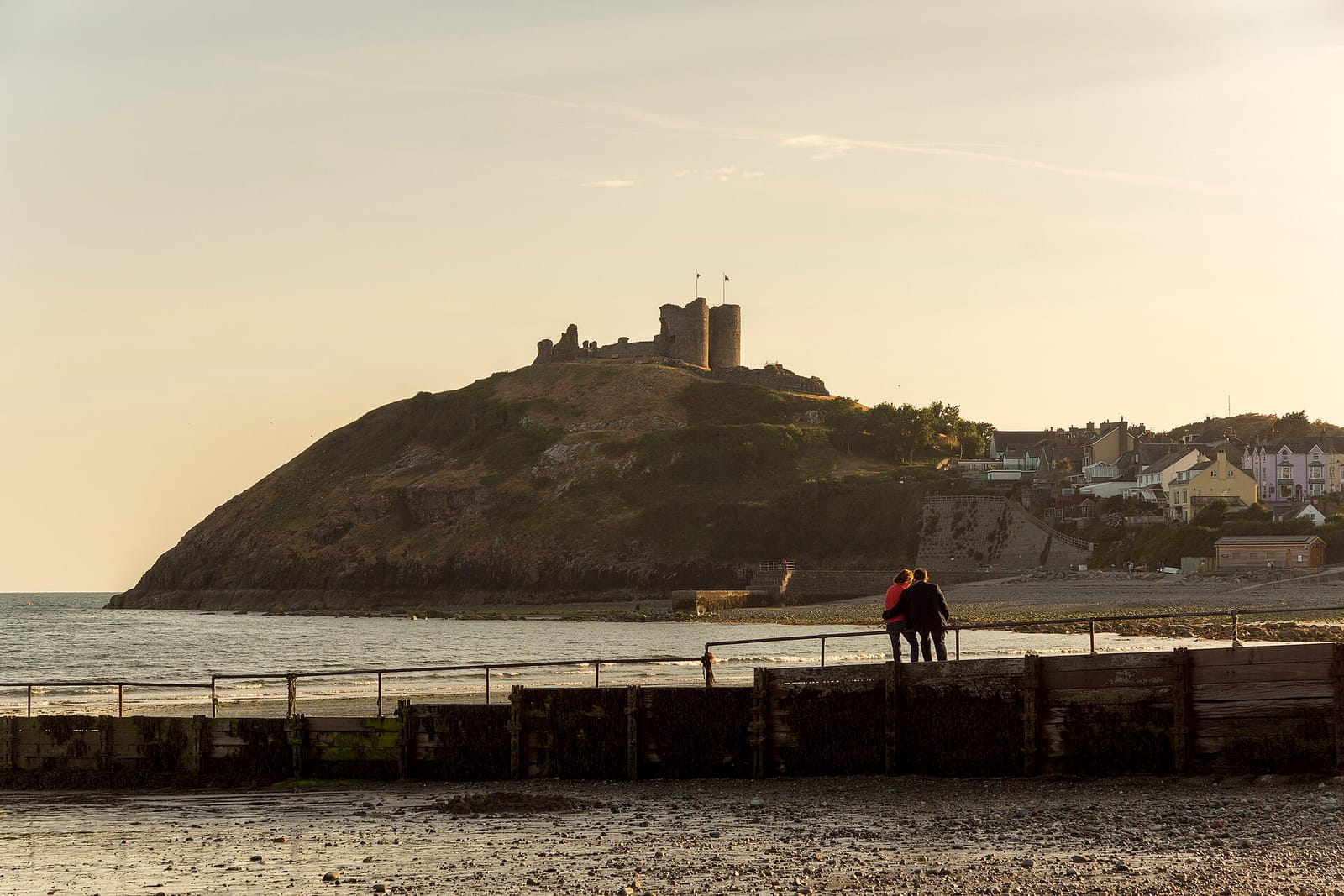 Criccieth Castle on its green headland at sunset above the beach